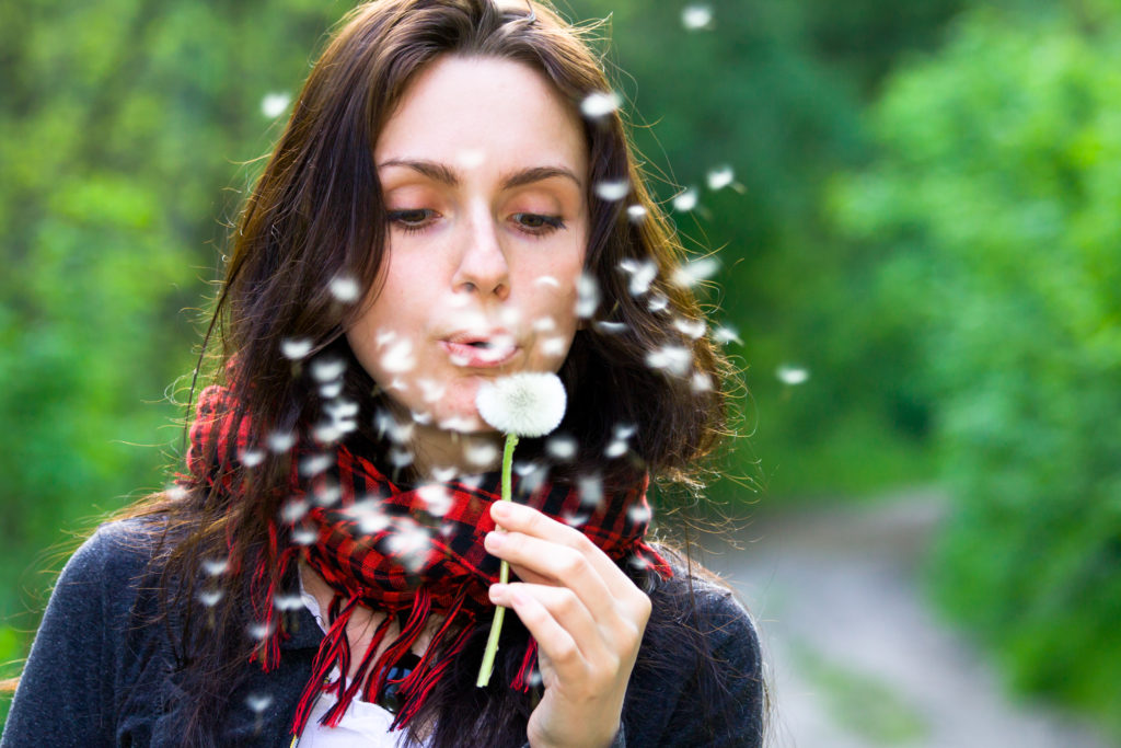 a woman blowing on a dandelion while traveling with allergies